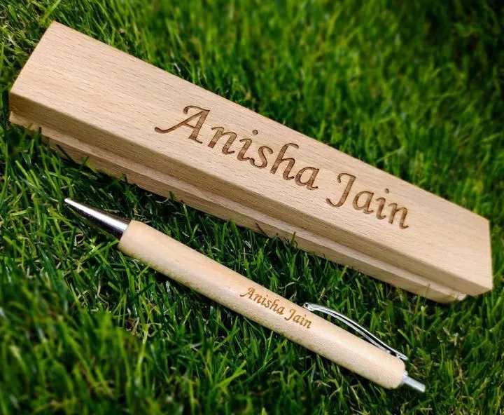 Wooden ball pen engraved with a name lying on grass beside a wooden box