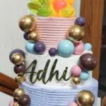 Cake with a gold acrylic name topper reading Adhi