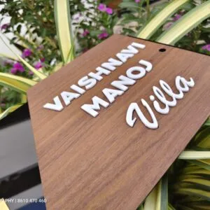 Wooden name board with raised white 3D letters reading Vaishnavi Manoj Villa