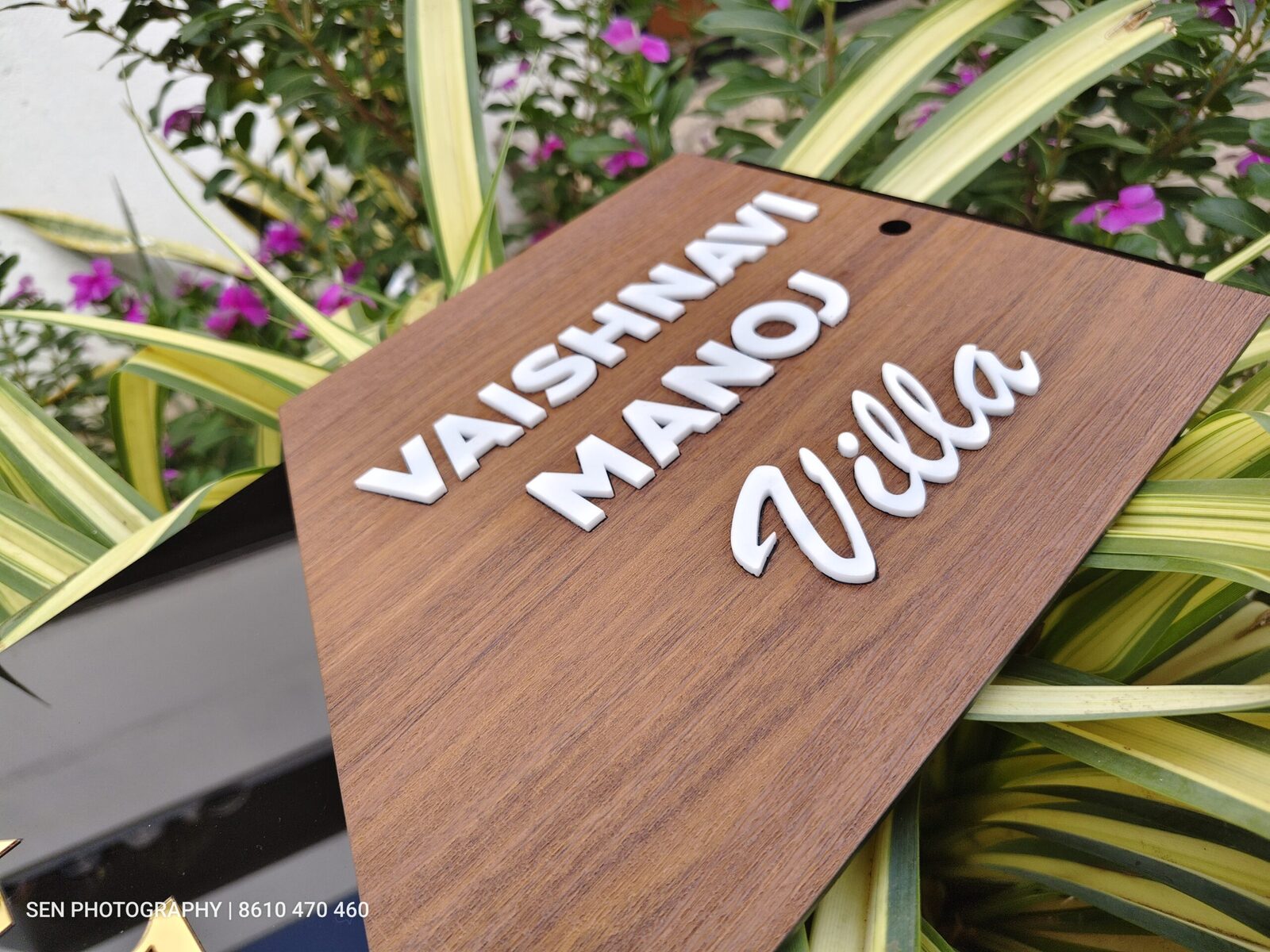 Wooden name board with raised white 3D letters reading Vaishnavi Manoj Villa