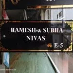 Black and gold acrylic name plate reading Ramesh and Subha Nivas