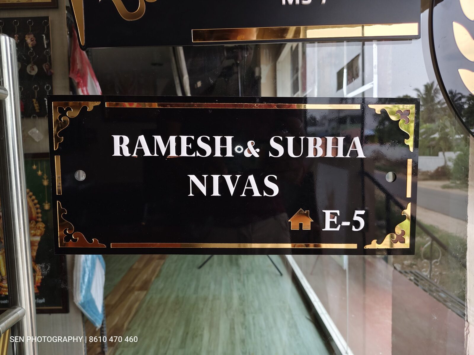 Black and gold acrylic name plate reading Ramesh and Subha Nivas