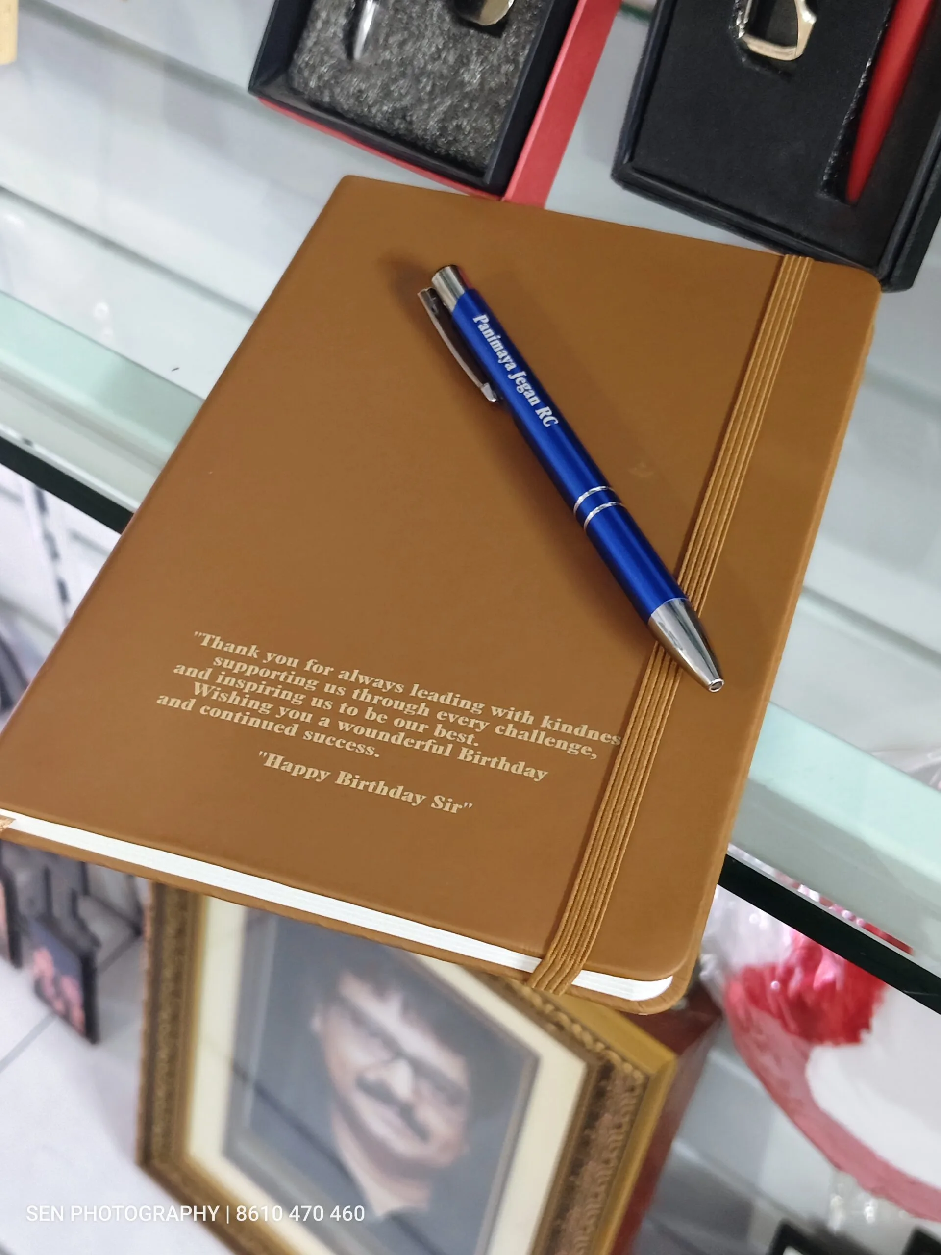 Tan hardbound notebook engraved with a message beside a personalised blue pen